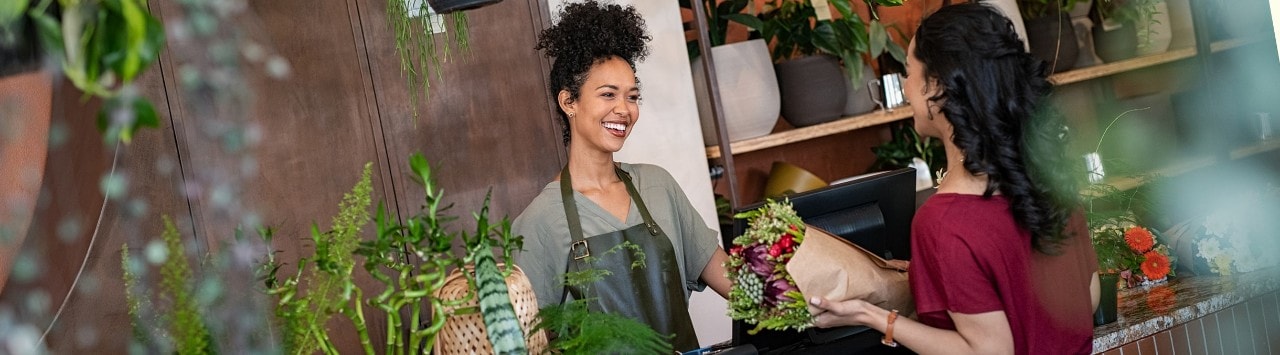 Happy female florist selling bouquet to female customer