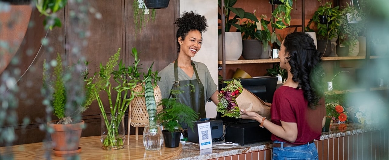 Happy female florist selling bouquet to female customer