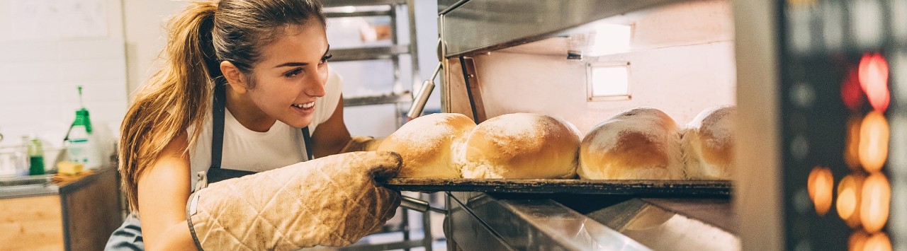 Young female baker taking bread out of oven