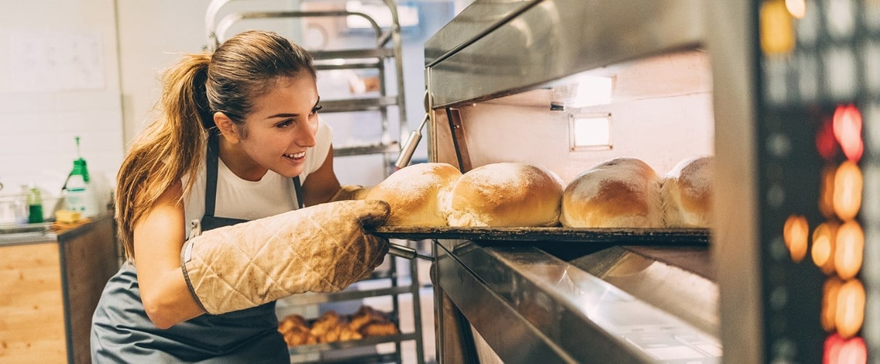 Young female baker taking bread out of oven