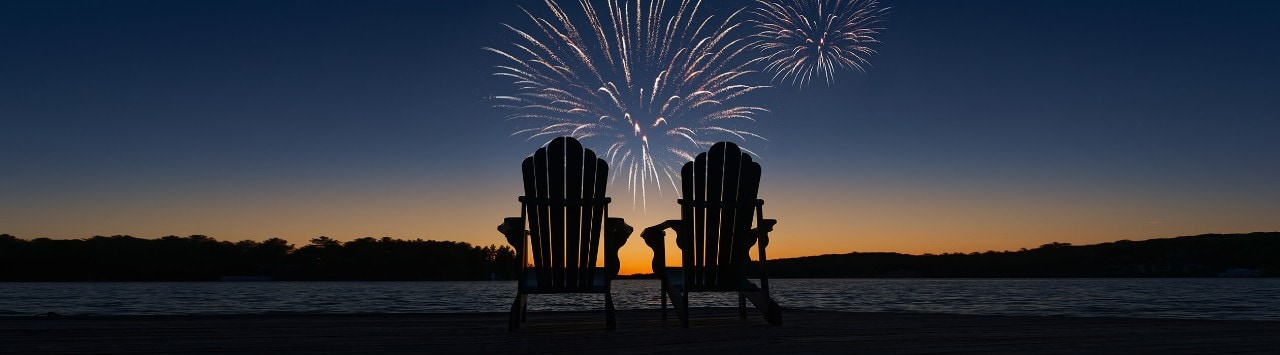 Two empty Adirondack chairs in front of a twilight fireworks display