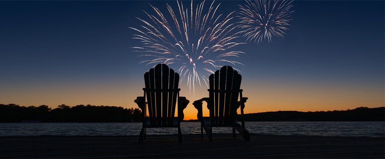 Two empty Adirondack chairs in front of a twilight fireworks display