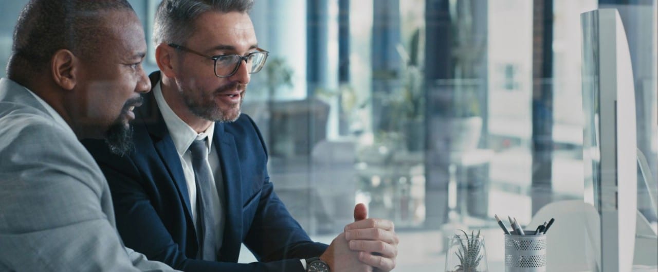 Two businessmen wearing suits, in discussion, facing a laptop in an office
