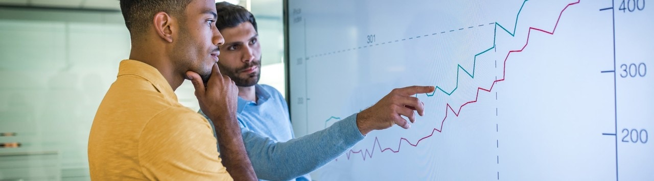 Diverse businessmen reviewing business growth on large screen line graph