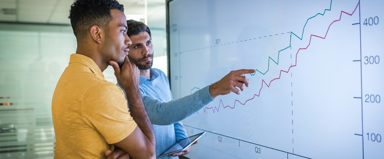 Diverse businessmen reviewing business growth on large screen line graph