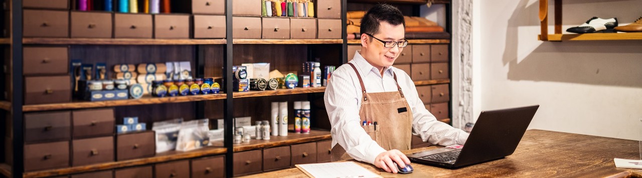 Asian-American shoe store owner using laptop on counter