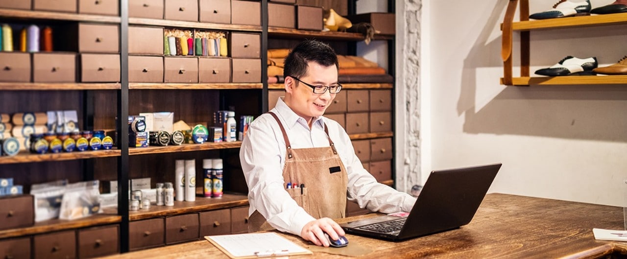 Asian-American shoe store owner using laptop on counter