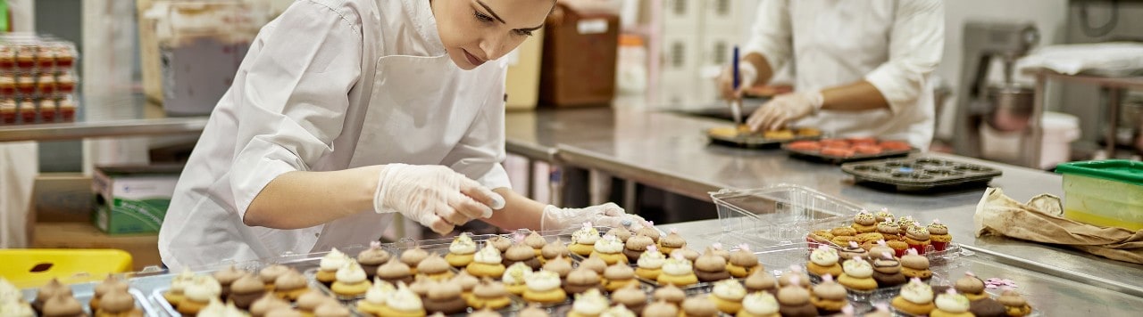 Female professional baker icing large order of cupcakes