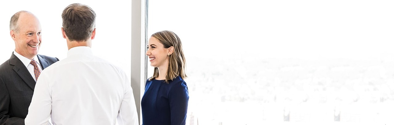 Three businesspeople in a conversation standing in front of a window