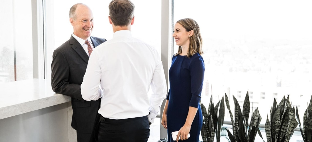 Three businesspeople in a conversation standing in front of a window