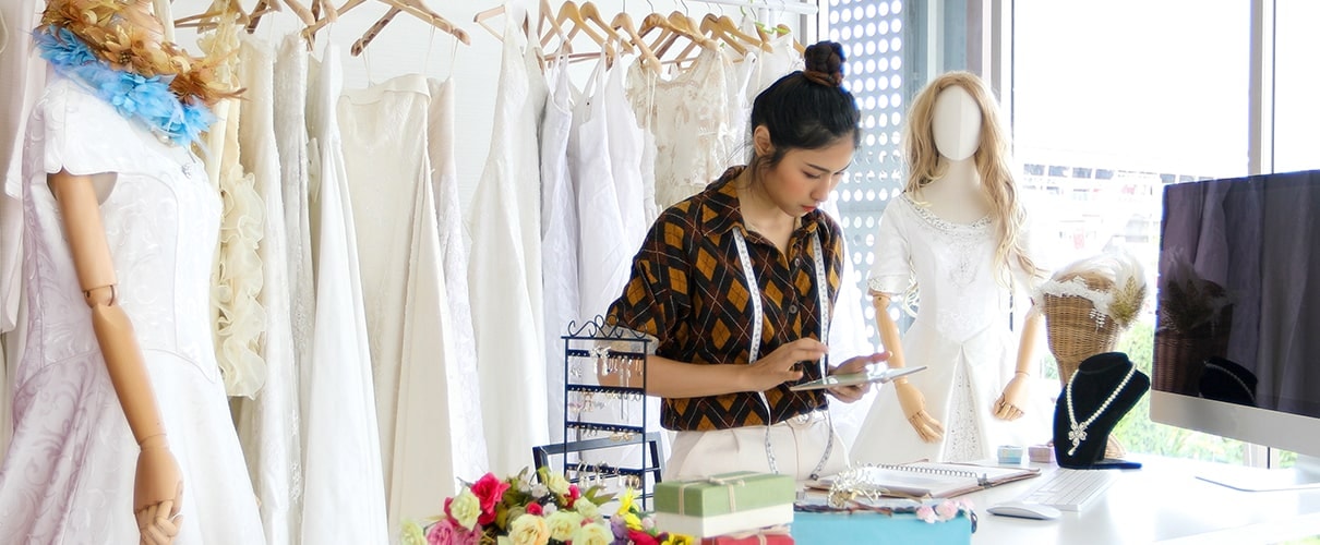 women Fashion Designer Working and using smart phone and tablet With Wedding Dresses at at clothing store