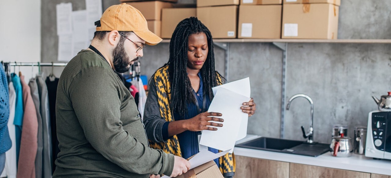 Caucasian man and African-American woman arranging customer orders for drop-shipping in warehouse.