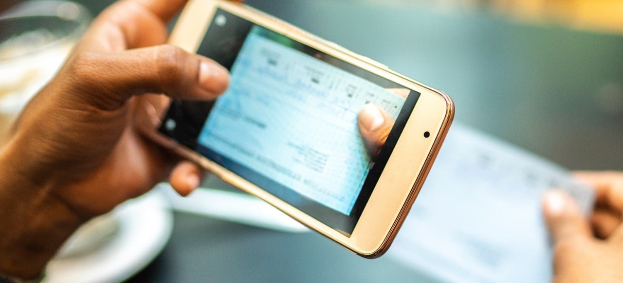 Young woman depositing check by phone in the cafe