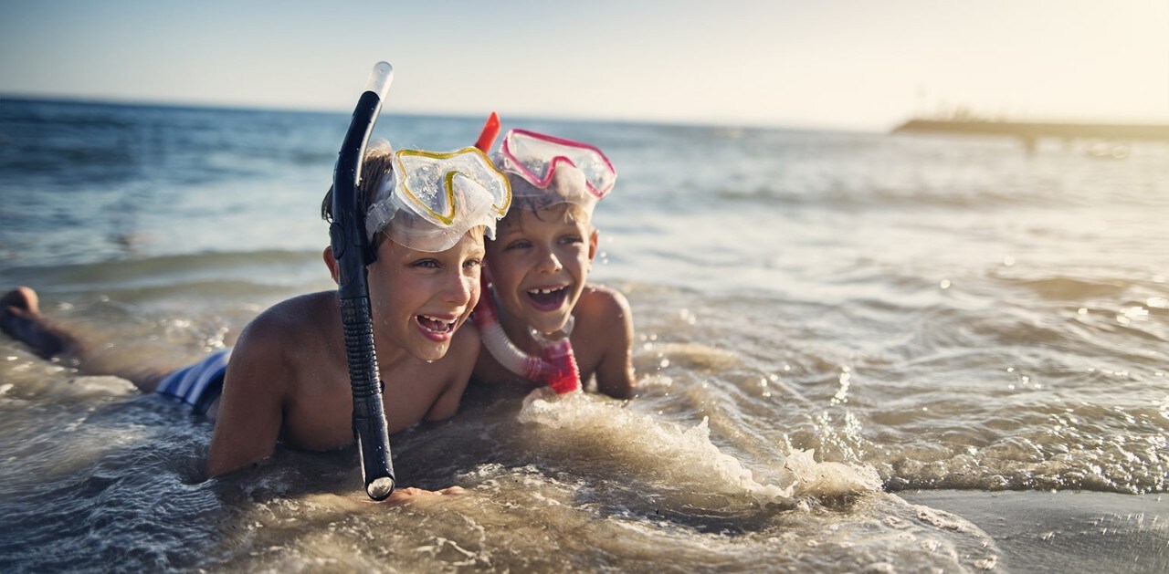 Two young brothers wearing snorkeling masks laying in ocean waves