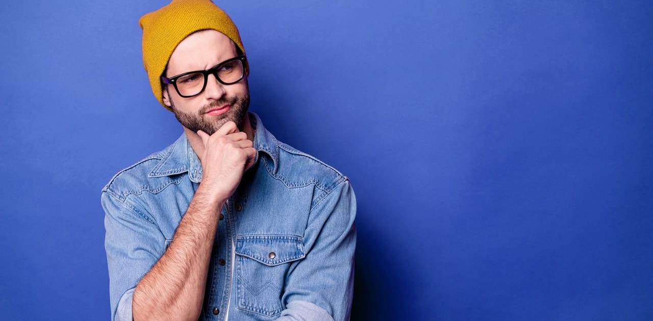 Man wearing yellow ski cap holding hand to chin with a perplexed, questioning look