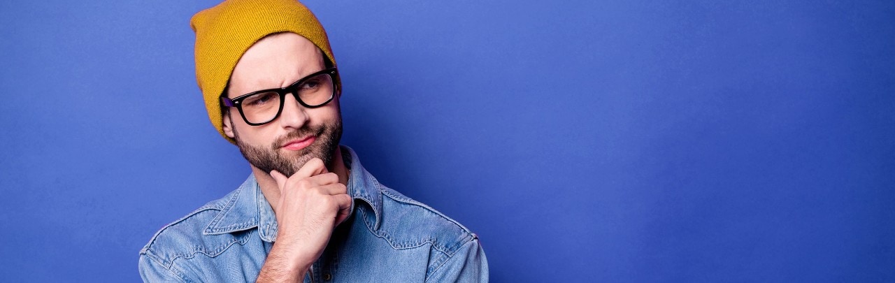 Man wearing yellow ski cap holding hand to chin with a perplexed, questioning look