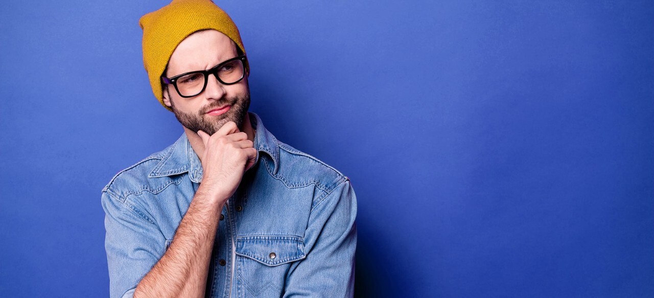 Man wearing yellow ski cap holding hand to chin with a perplexed, questioning look
