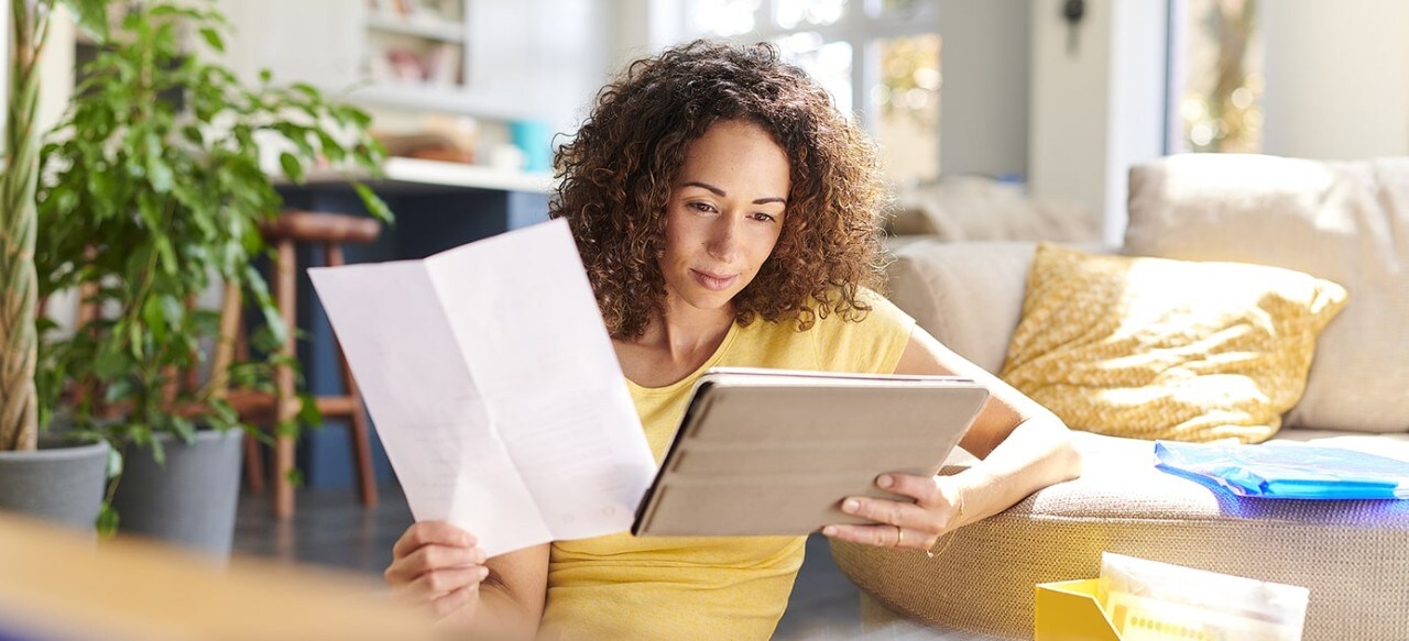 African-American woman holding financial paper and looking at tablet