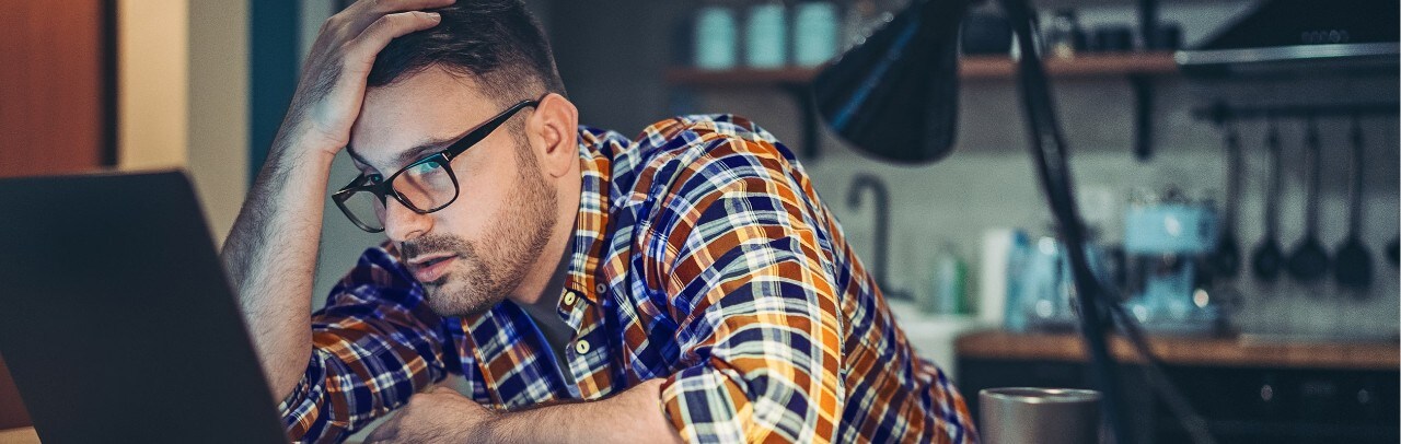 Frustrated man looking at computer with hand on his head