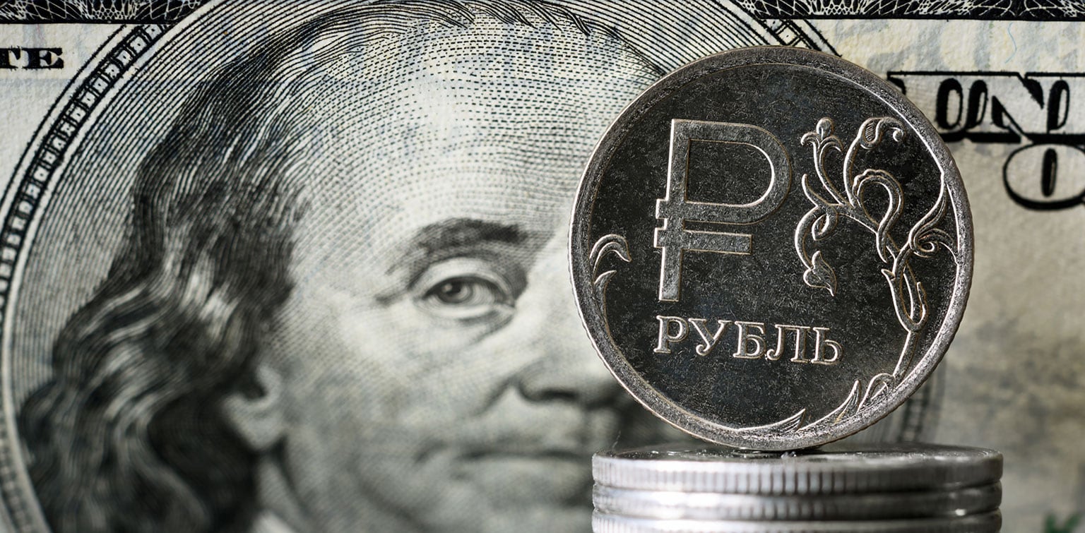 Russian Ruble coins with an American $100 bill in the background