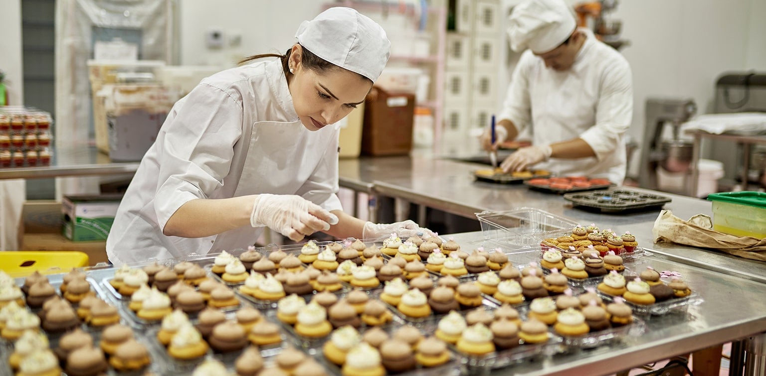 Female professional baker icing large order of cupcakes