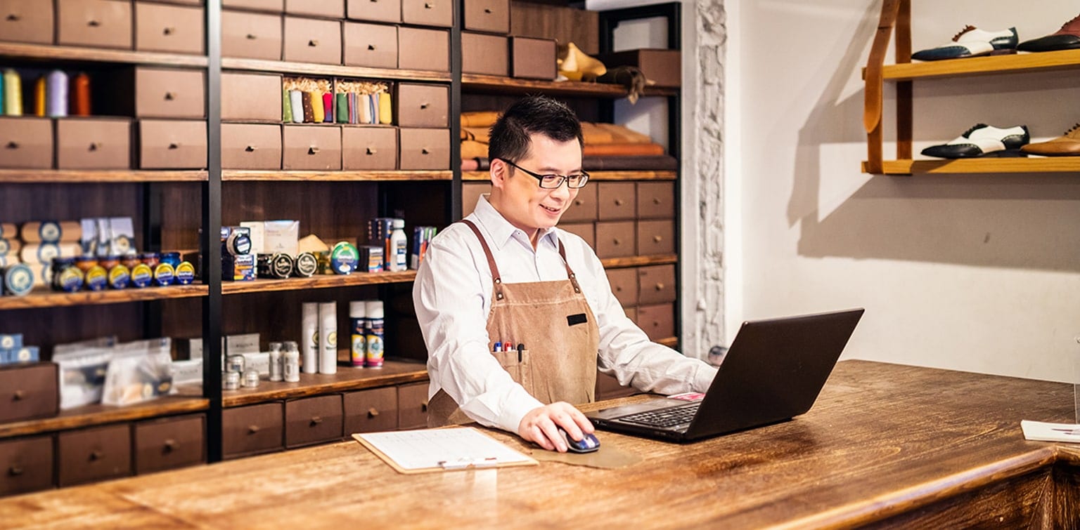 Asian-American shoe store owner using laptop on counter
