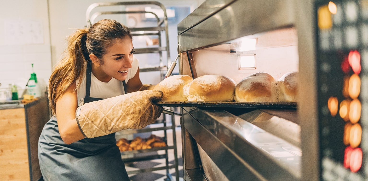 Young female baker taking bread out of oven