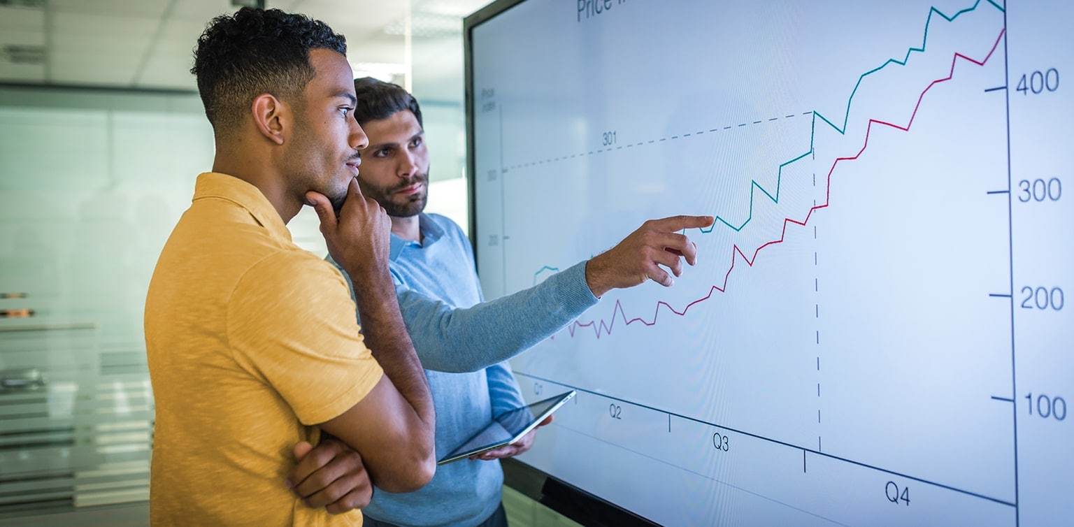 Diverse businessmen reviewing business growth on large screen line graph