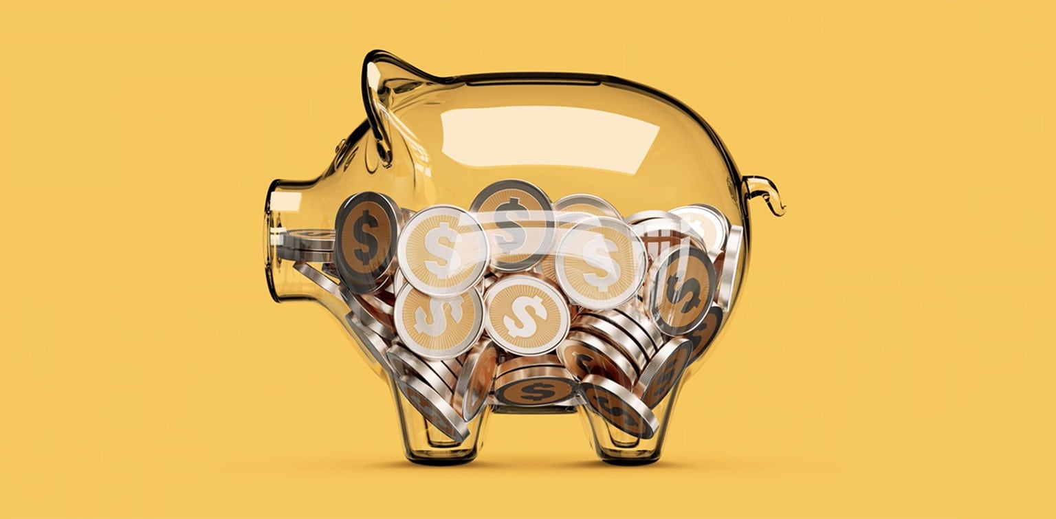 lear piggy bank full of coins in front of yellow background.