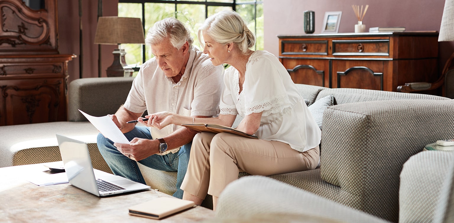 Senior couple reviewing financial documents with laptop