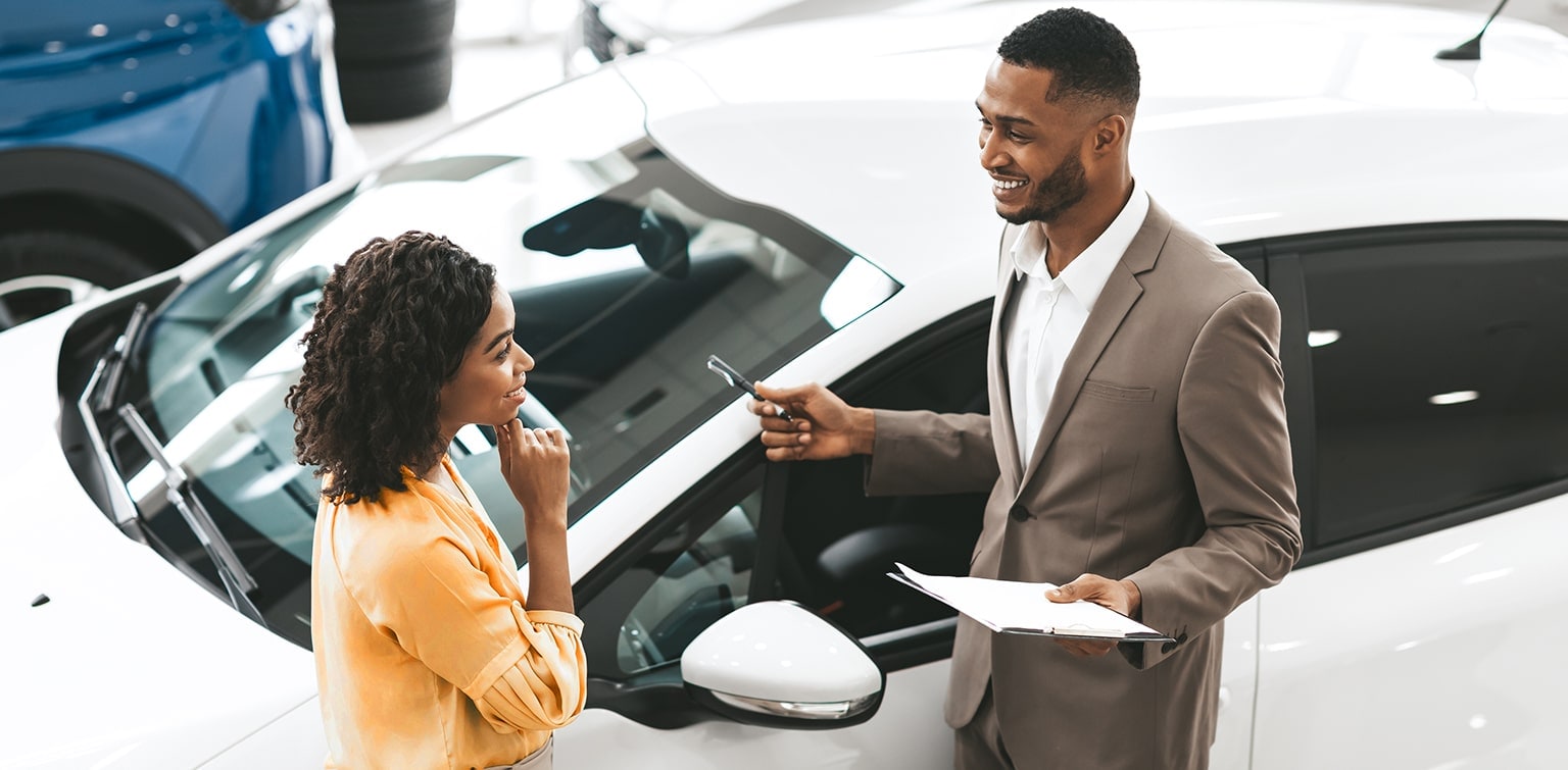 African-American car salesman talking to African-American female customer standing in front of white car