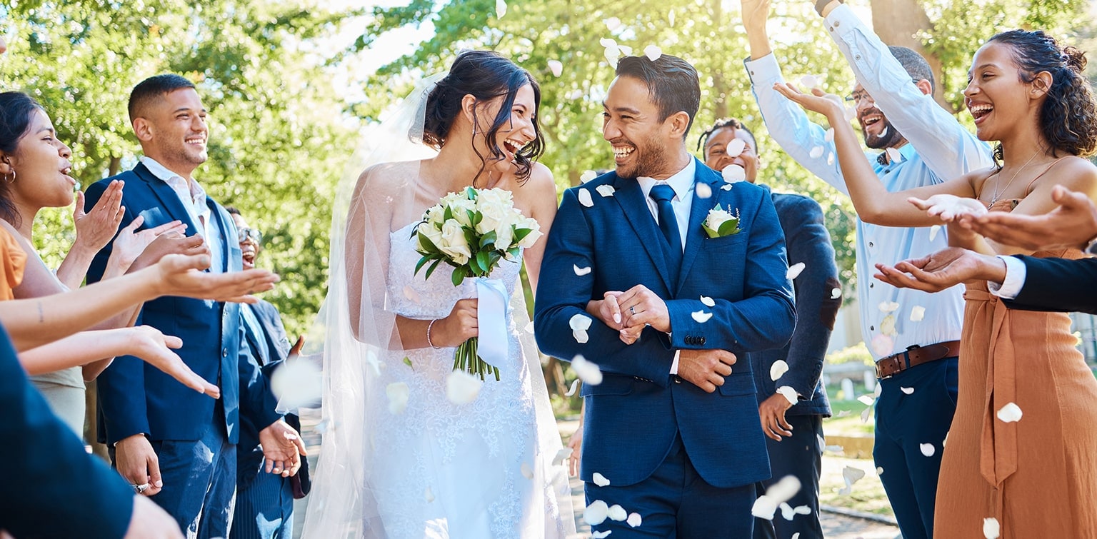 Happy married couple walking down the aisle while guests throw rose petals