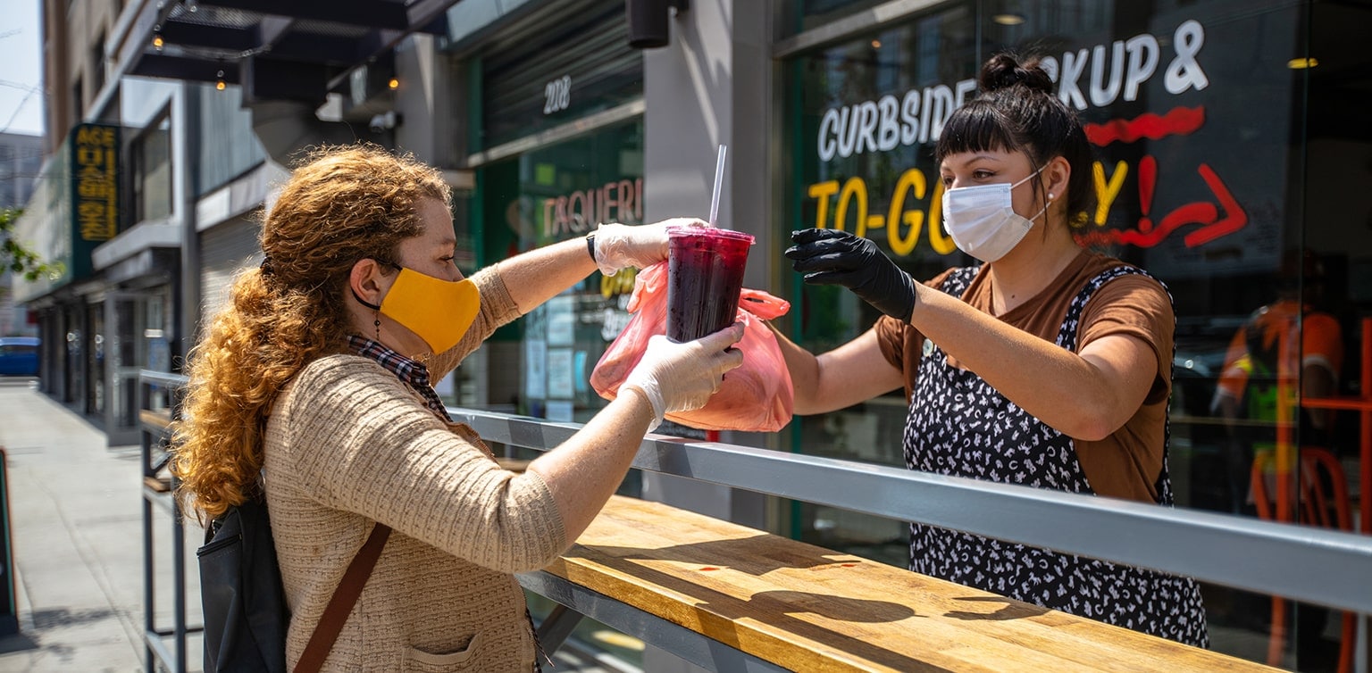 Masked restaurant employee hands order to customer at curbside pick-up