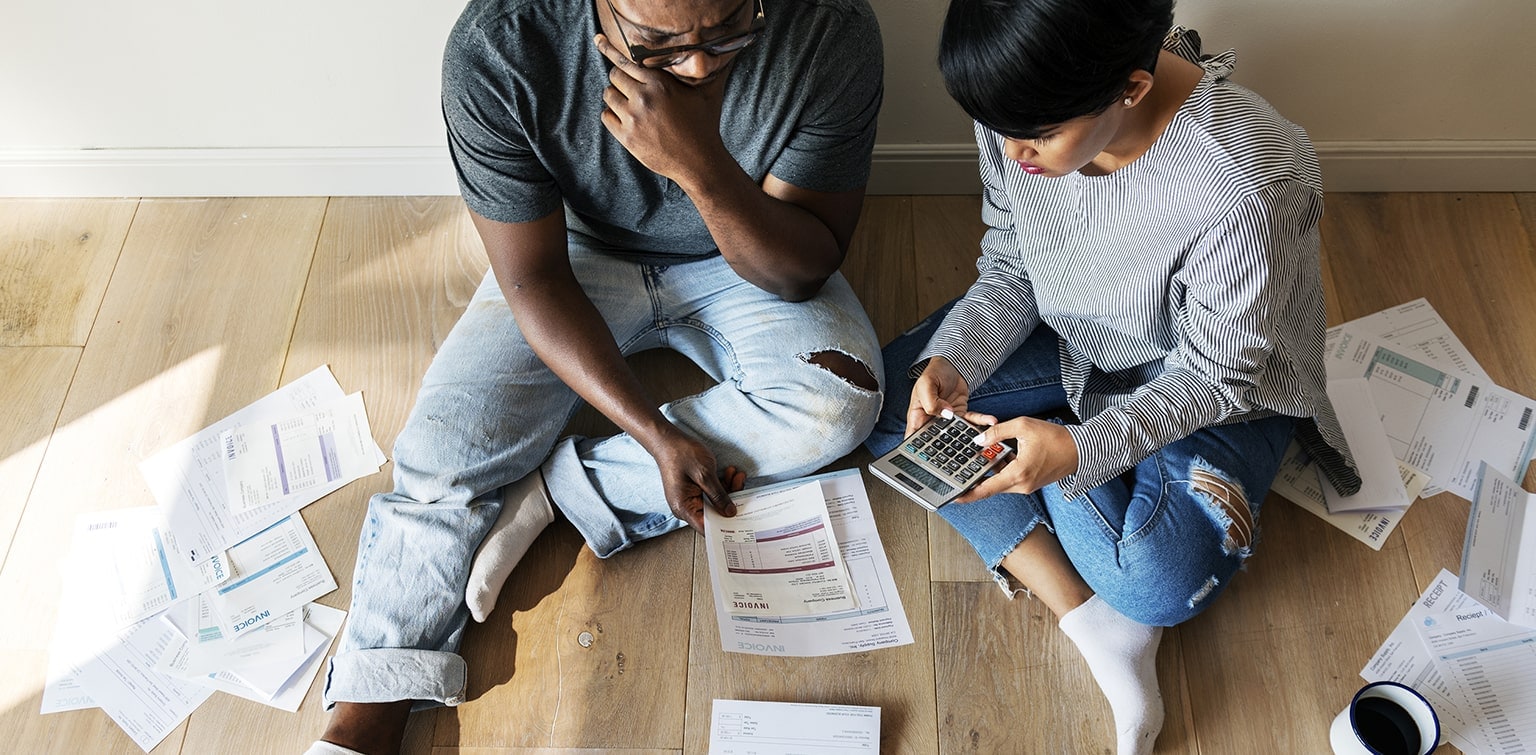 Couple sitting on floor reviewing bills and calculating debt