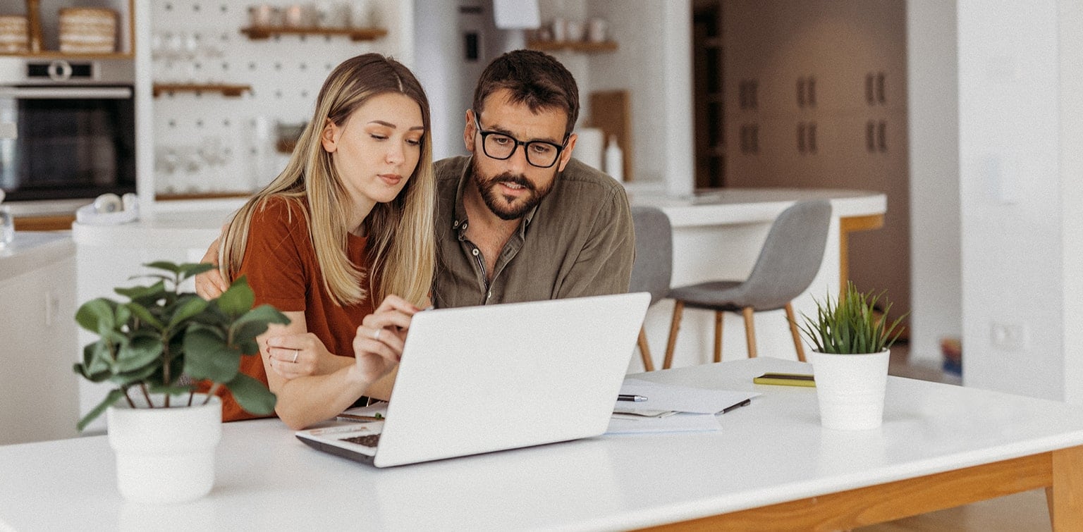 Couple at kitchen table paying bills on laptop