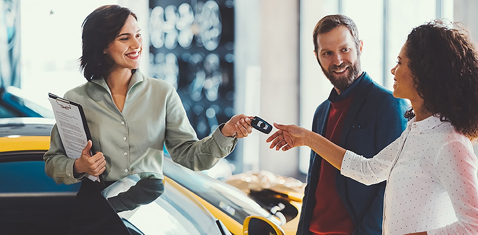 Car saleswoman handing keys to multiracial couple