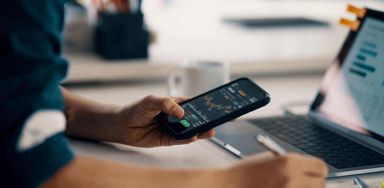 Man reviewing financial data on smartphone and laptop