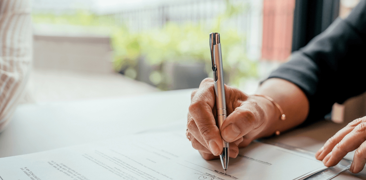 Person signing financial documents with a pen during a professional meeting