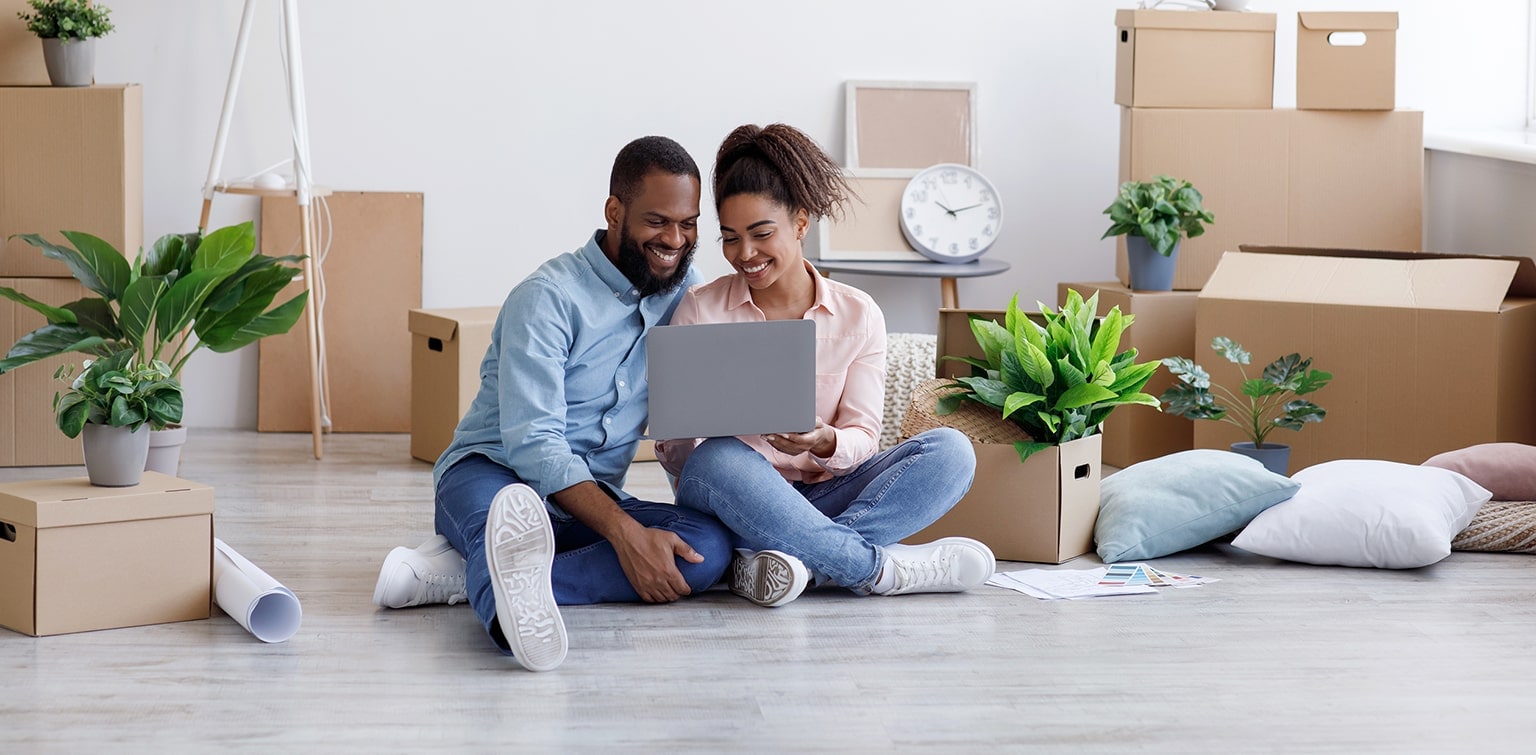 Young African-American couple sitting on floor using laptop surrounded by moving boxes