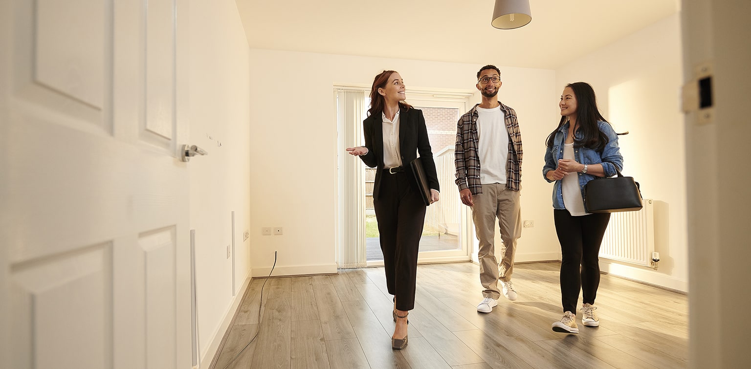 Happy young couple walking through empty home with realtor