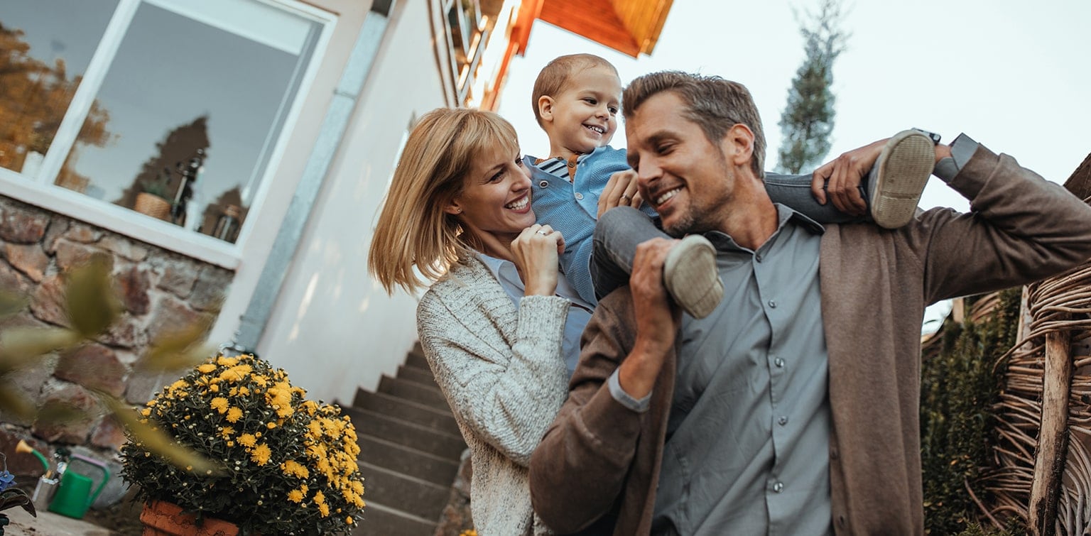 Mother holding child on father's shoulders in front of home