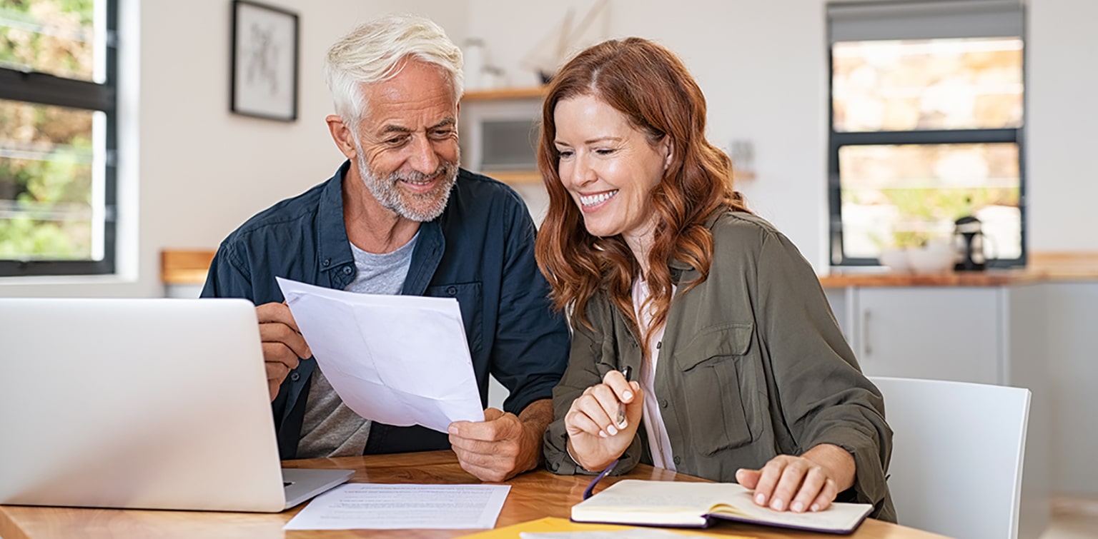 Couple sitting at table reviewing papers and using laptop