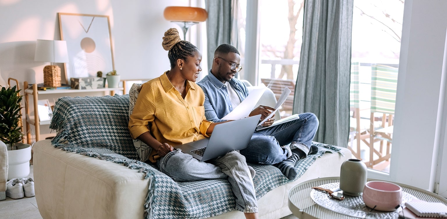 African-American couple sitting on couch reviewing financial documents