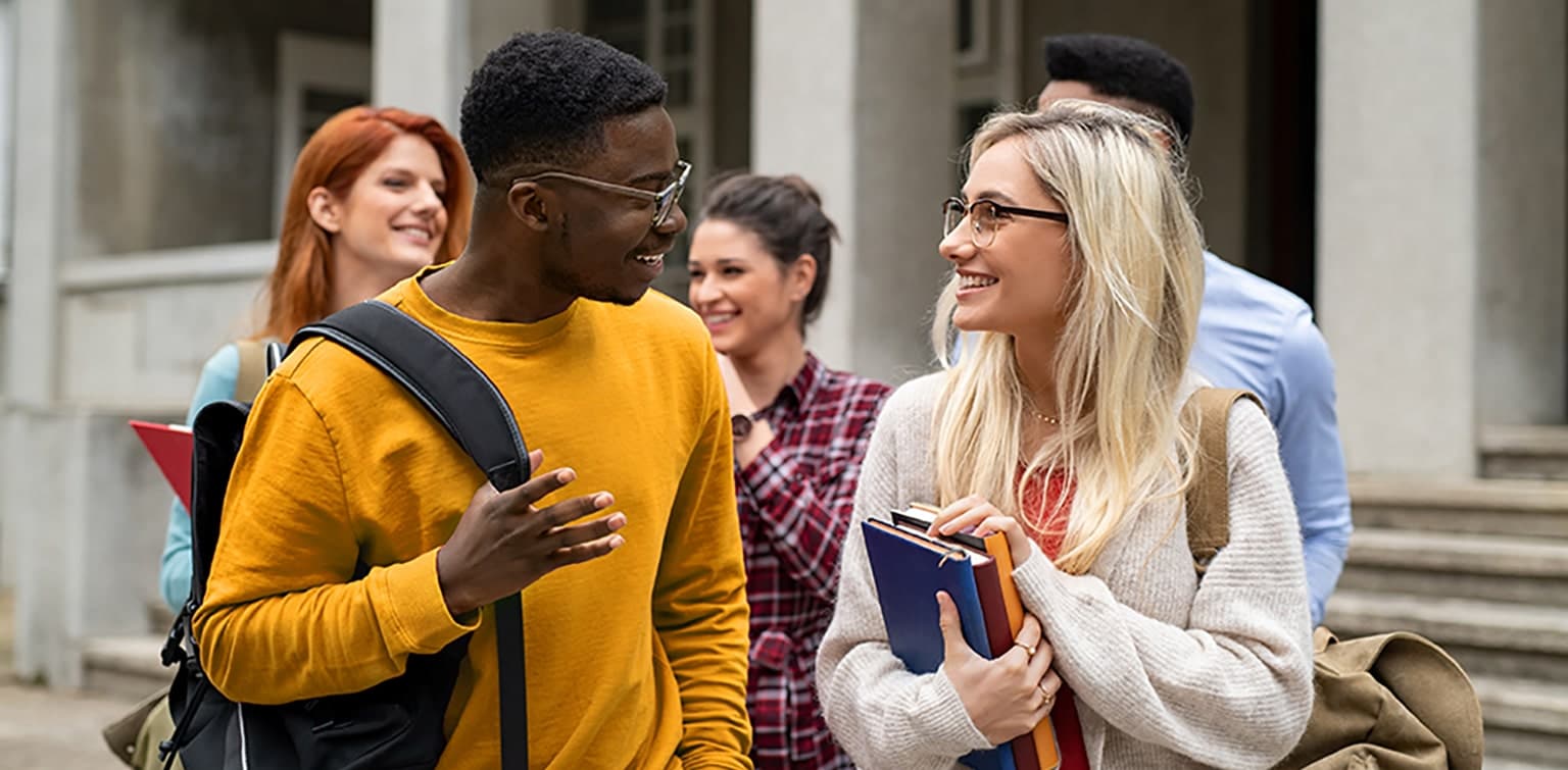 Diverse students carrying books and having conversation outside college building