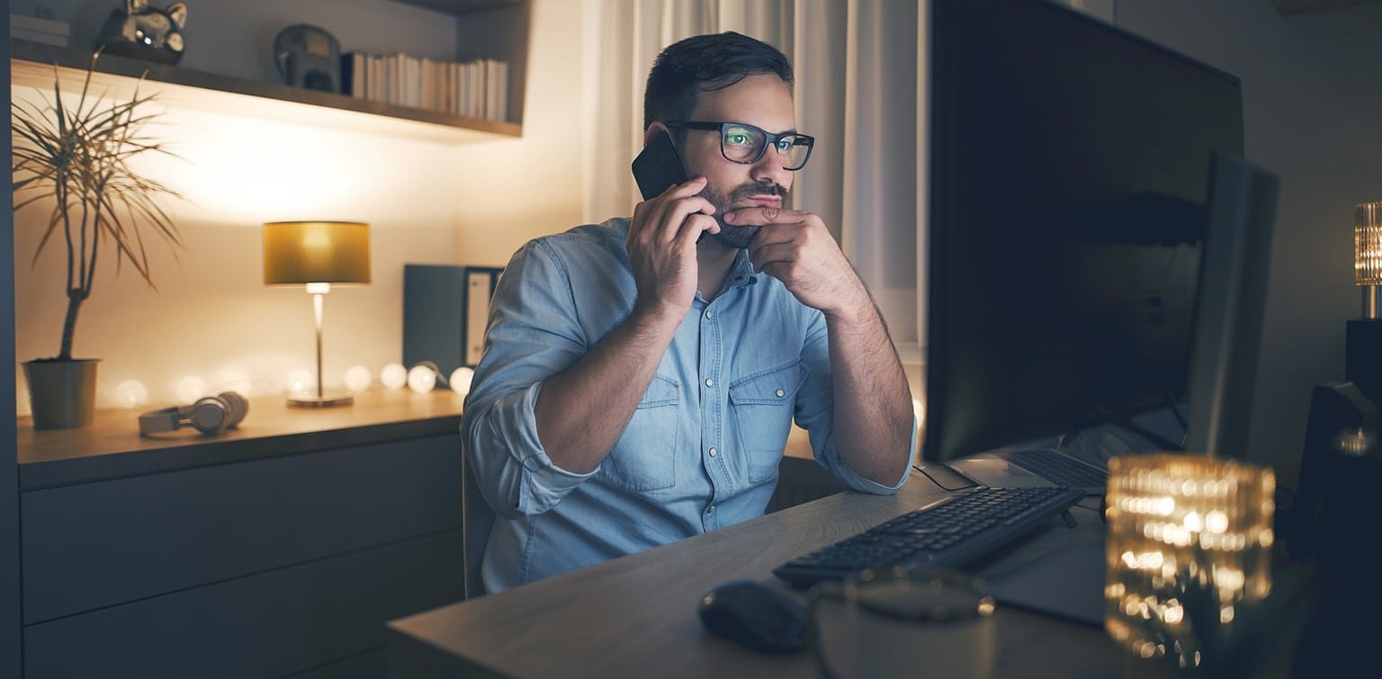 Concerned man talking on smartphone and looking at computer monitor