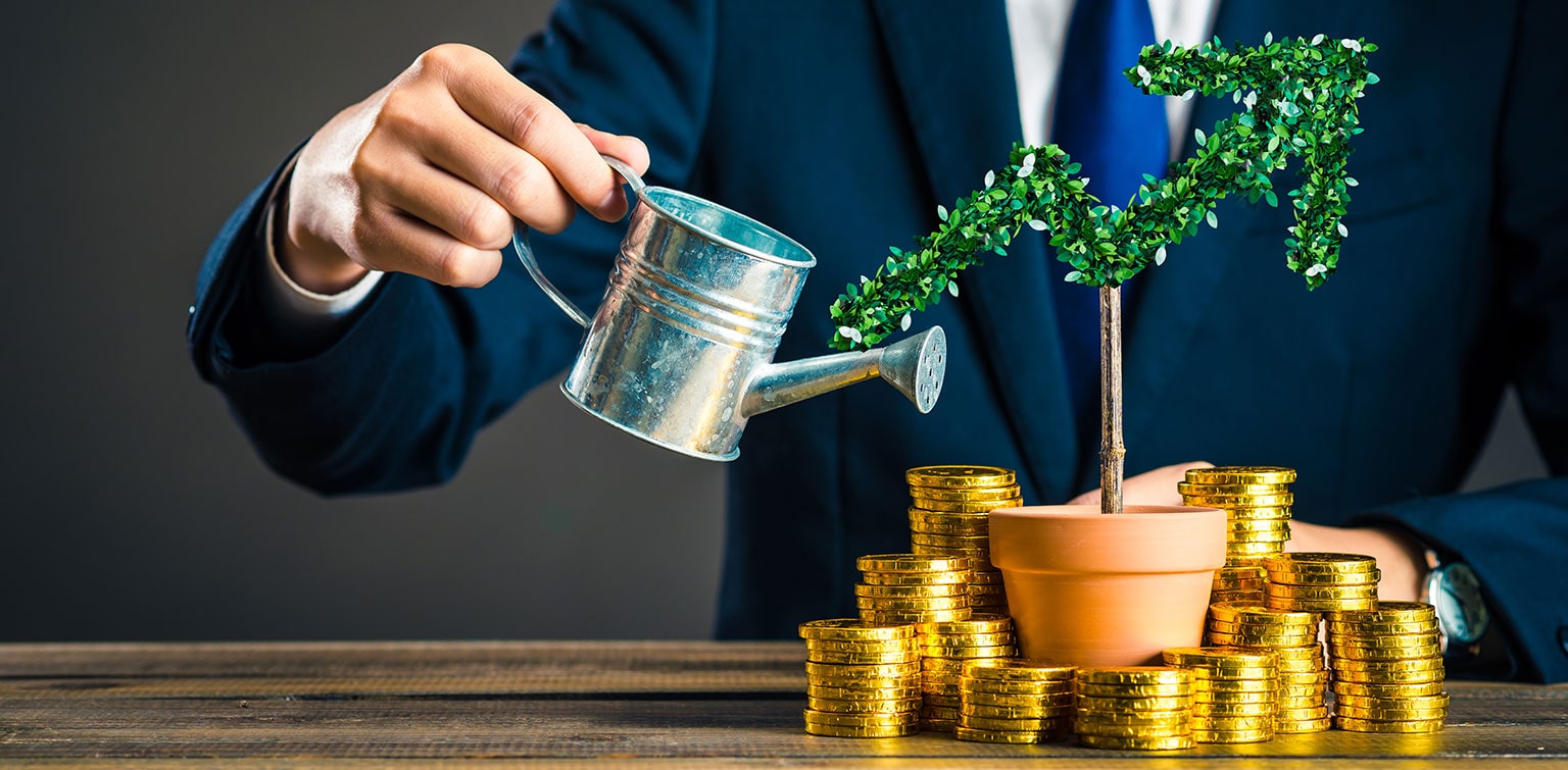 Businessman watering a tiny tree with a stack of coins at the base showing how he plans to grow wealth safely