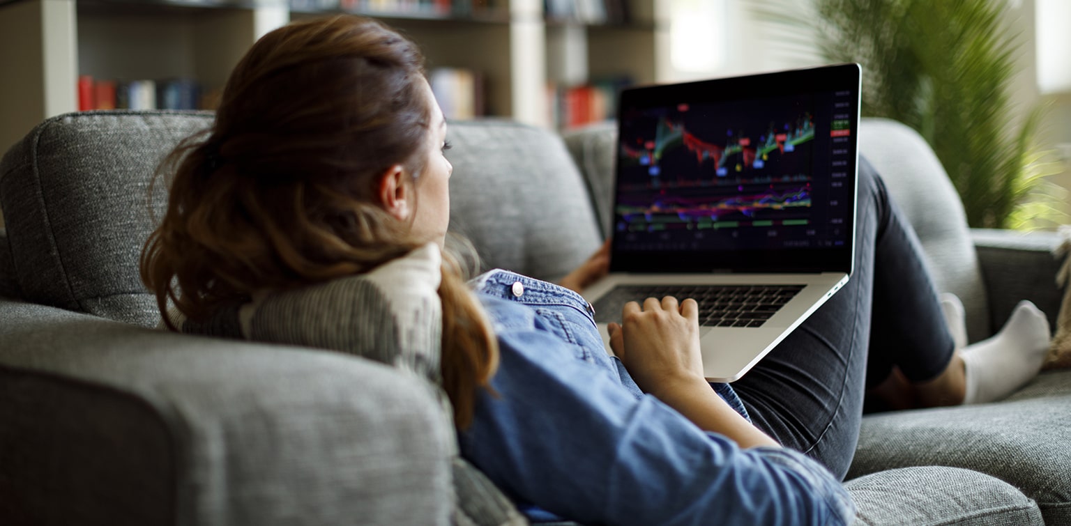 Woman on couch reviewing financial data on laptop