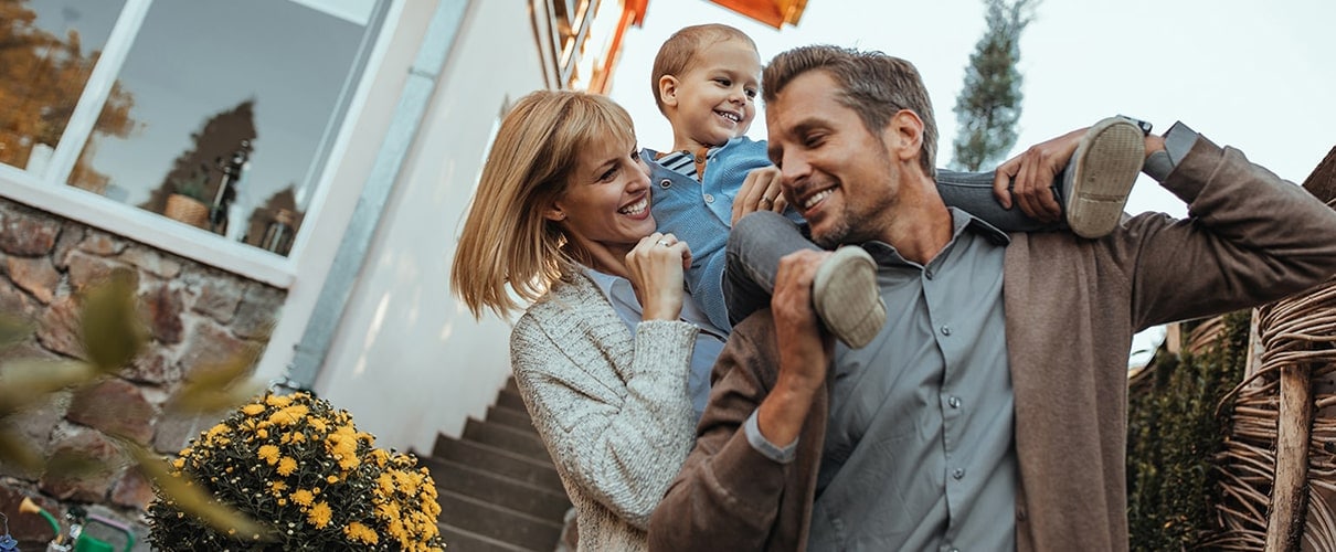 Mother holding child on father's shoulders in front of home