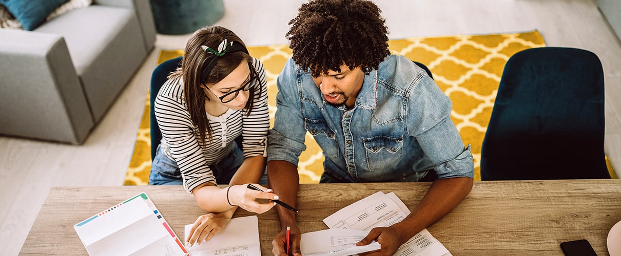 Diverse couple sitting at table reviewing financial documents