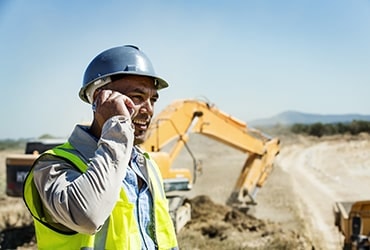 Hispanic construction foreman talking on phone standing in front of a bulldozer